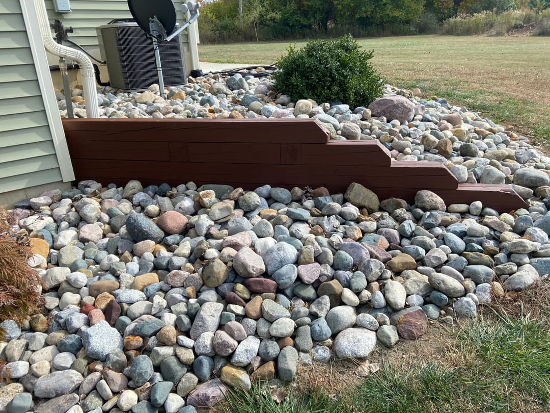 Decorative stone landscaping with wooden border near house foundation and grassy area.