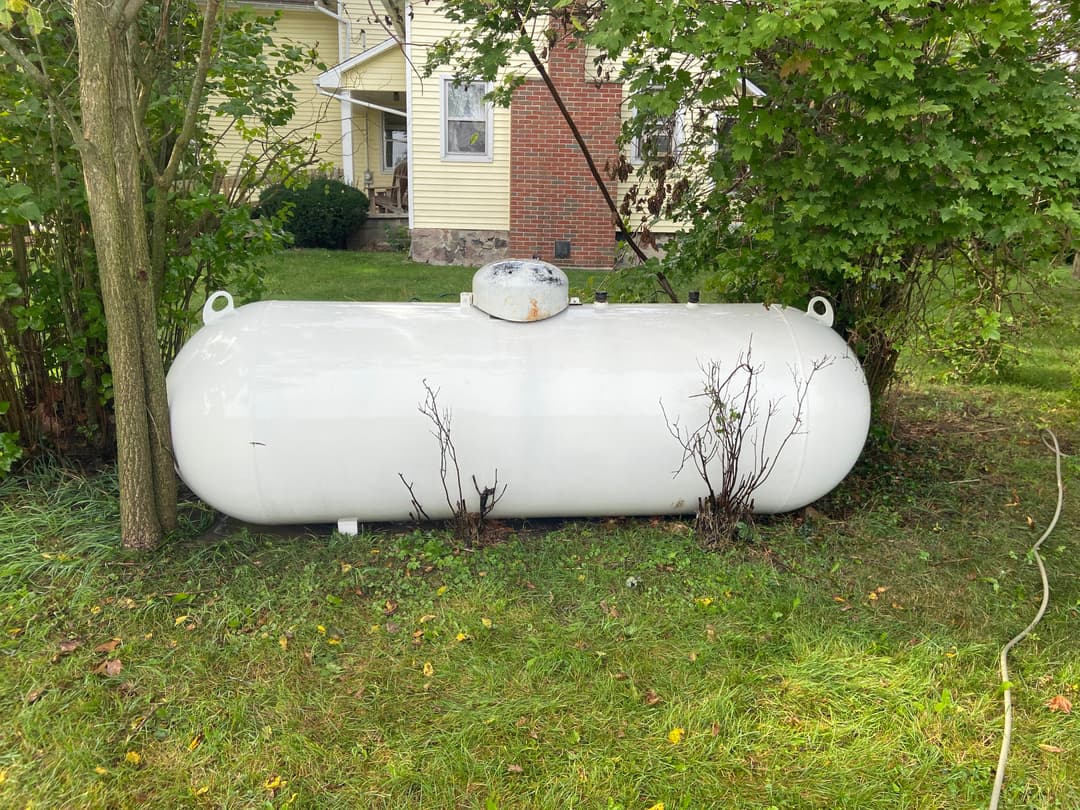 White propane tank located in a residential backyard surrounded by greenery.