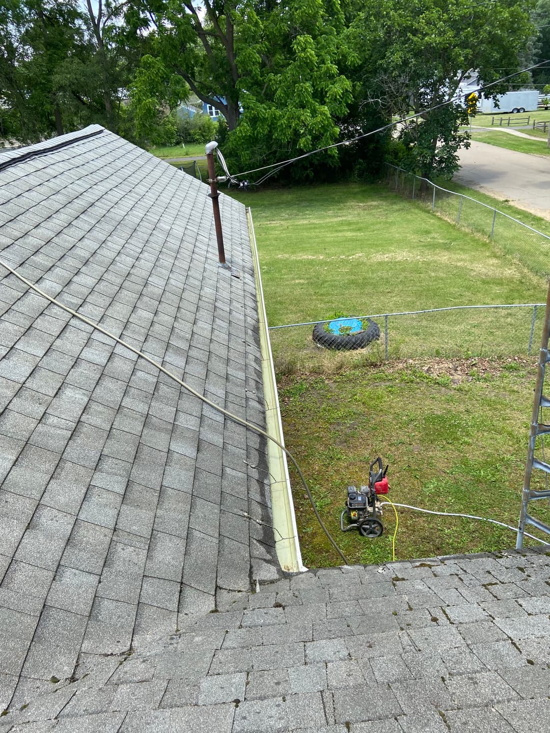 New roof installation with tools on sloped shingles and a clear yard view.
