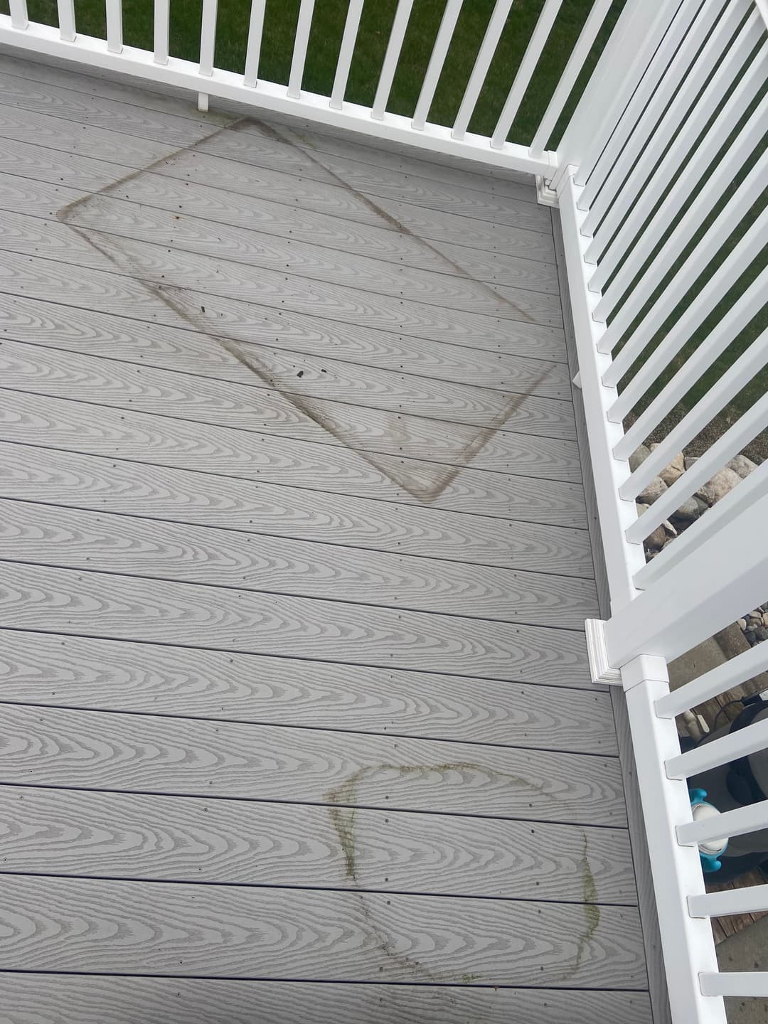 Stained deck with noticeable marks on composite flooring, featuring white railing and green grass.