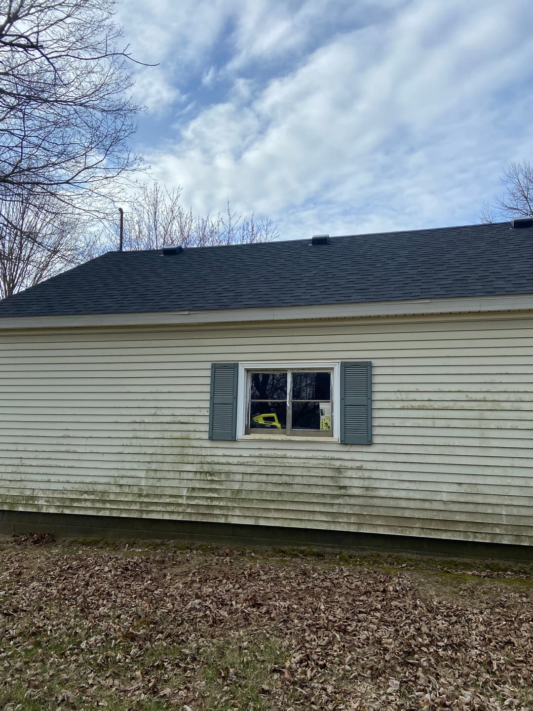 Exterior of a house with a window showing a yellow object inside, surrounded by fallen leaves.