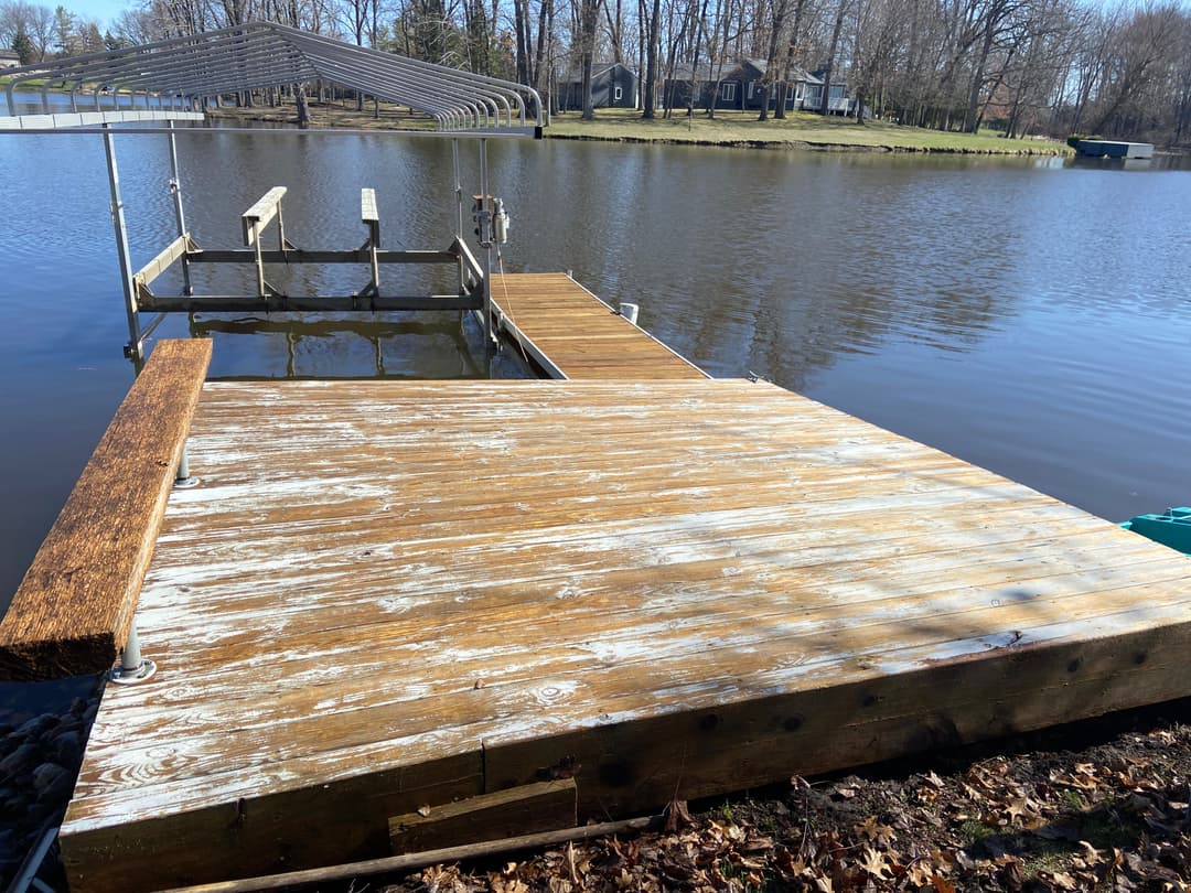 Wooden dock by a calm lake surrounded by trees, with a covered seating area.