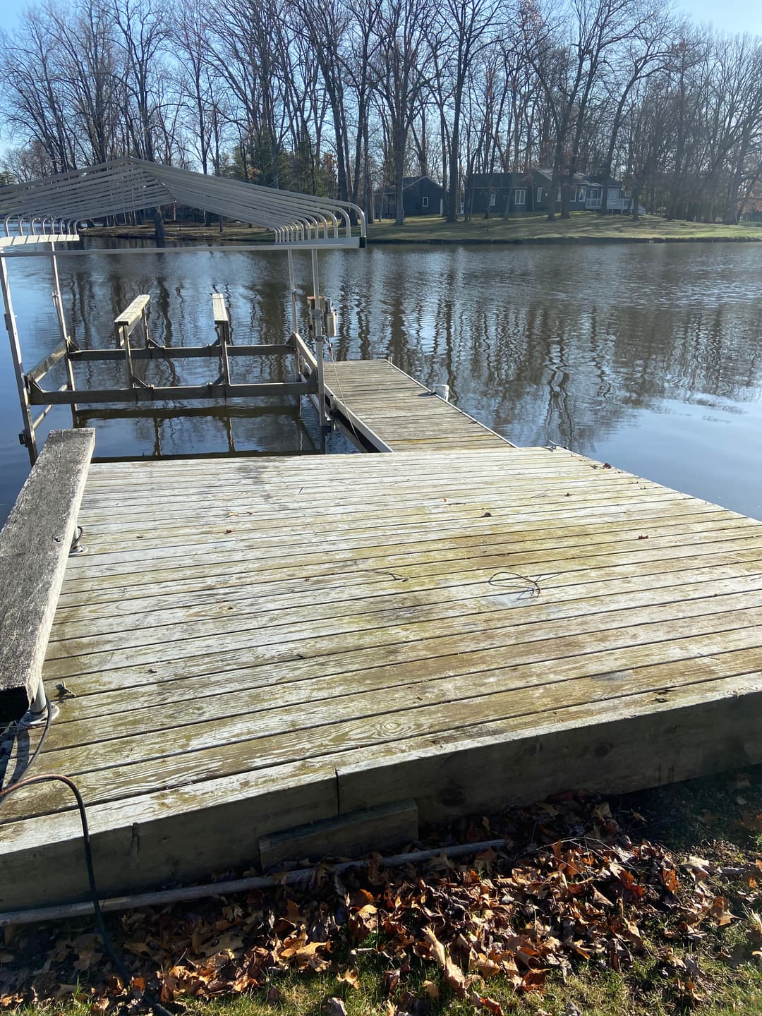 Wooden dock by a calm river with autumn leaves and trees in the background.