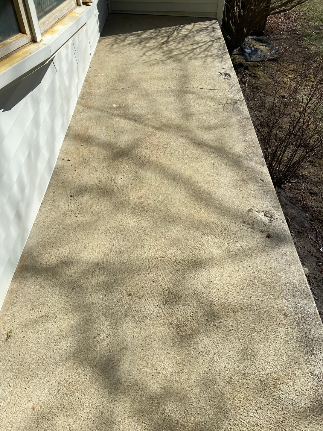 Sunlit concrete porch with shadows and a wooden house wall in the background.