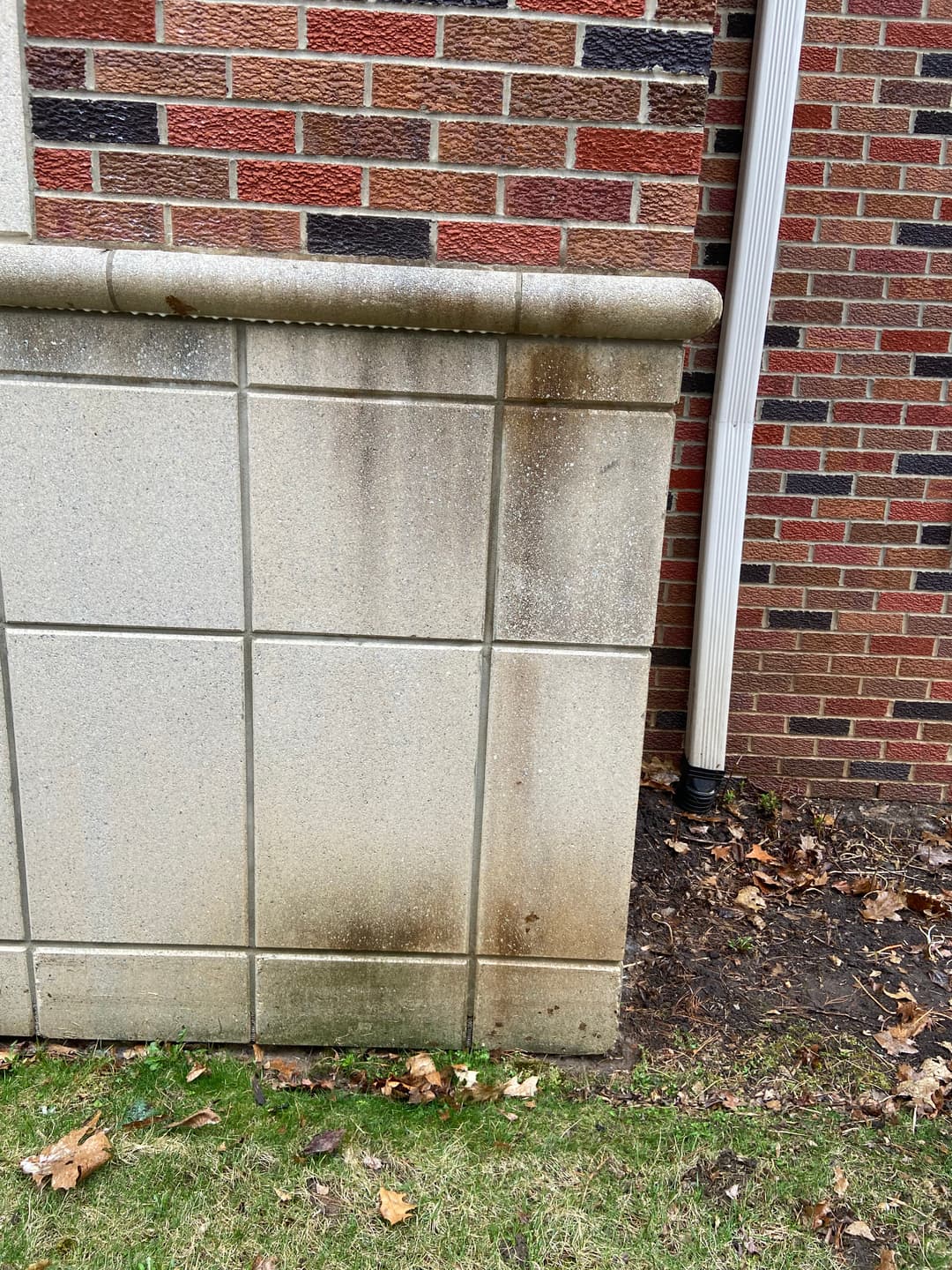 Weathered concrete wall with stains beside a brick building and downspout.