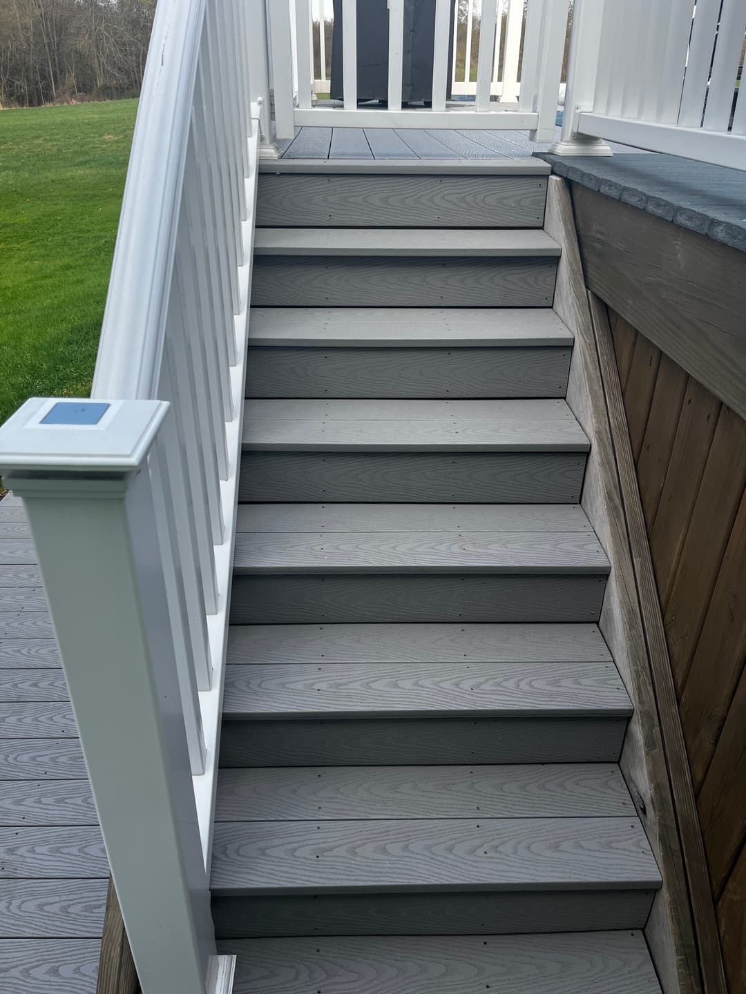 Wooden outdoor staircase leading to a deck, featuring white railing and grassy yard.